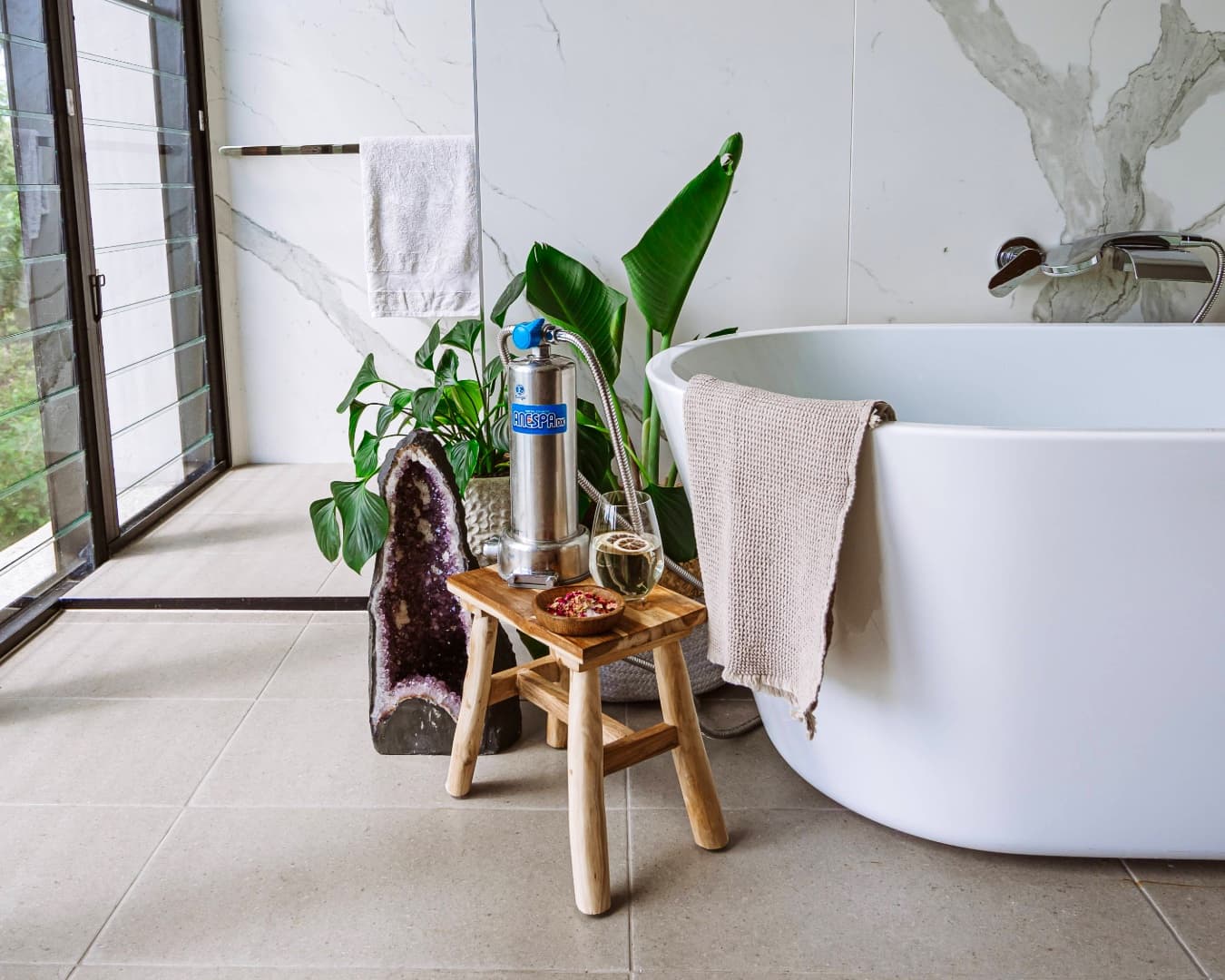 Enagic Anespa DX in a marble bathroom with floor-to-ceiling windows and a freestanding bathtub — the system treats both shower and bath water