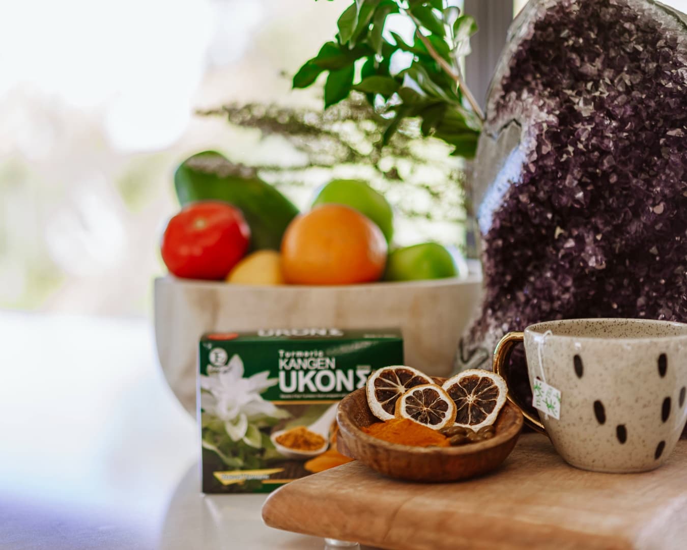 Kangen Ukon supplement box alongside dried turmeric, citrus slices, and a ceramic tea cup on a kitchen counter with natural light